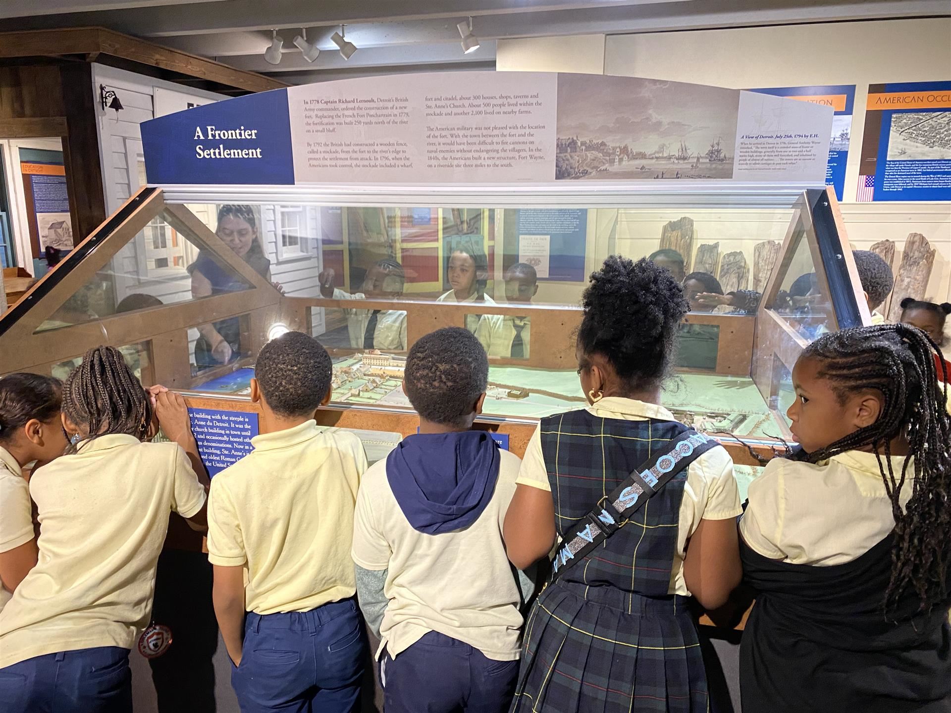 students standing around glass case of a replica of a frontier settlement